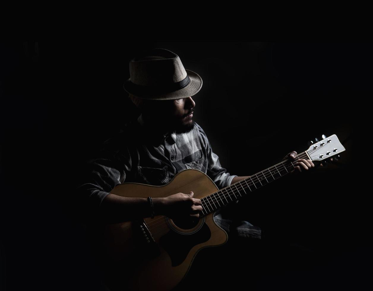 Young hipster guitarist on dark background photo