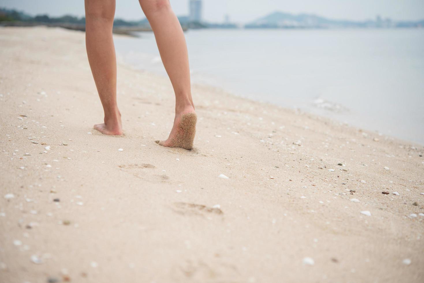 Mujer joven caminando sobre la arena de la playa dejando huellas en la arena foto