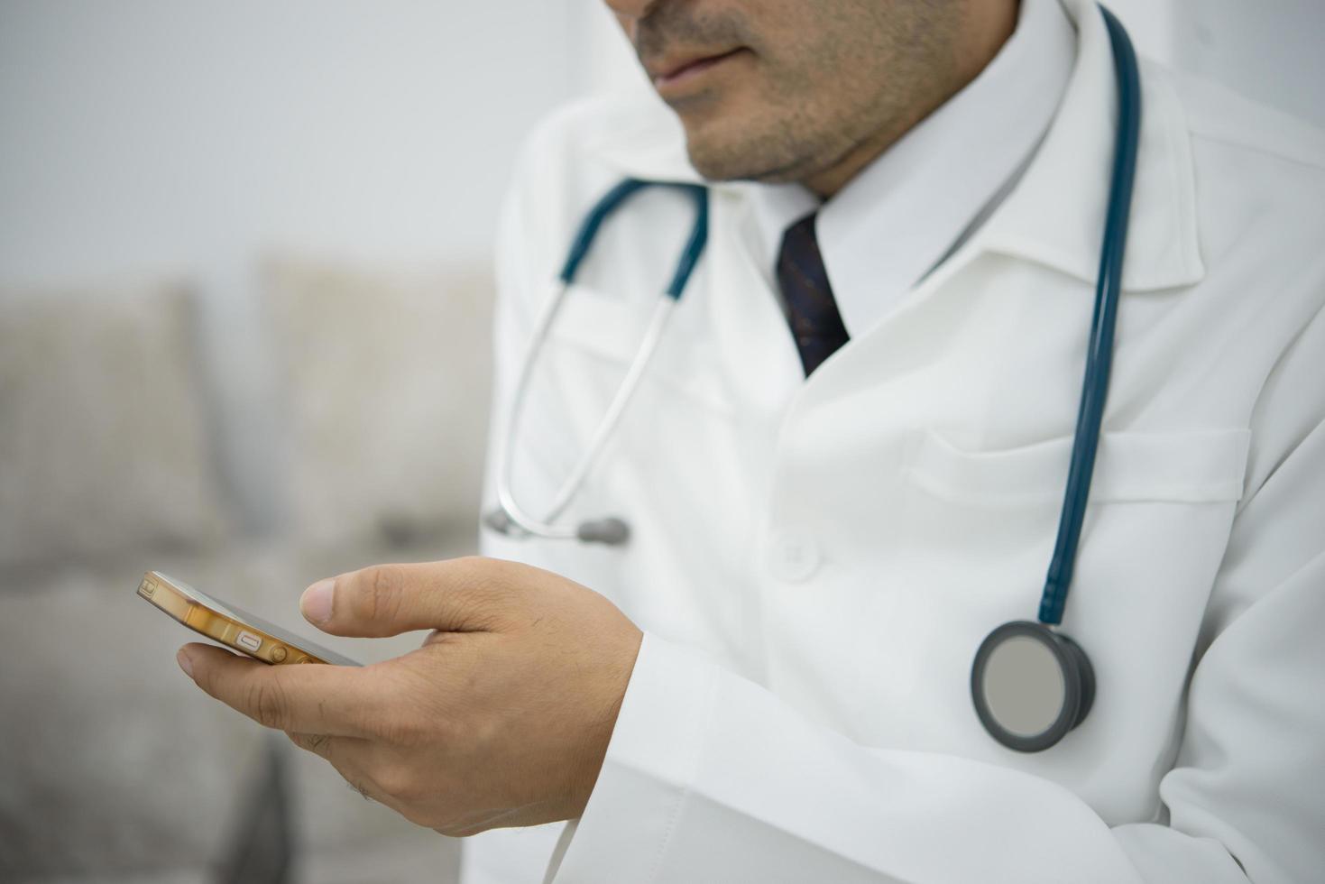 Male doctor in white coat using a smartphone device with touch screen photo