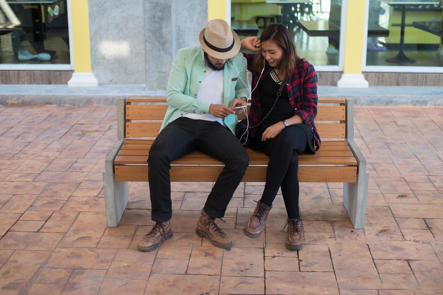 Pareja hipster escuchando música juntos mientras está sentado en un banco foto