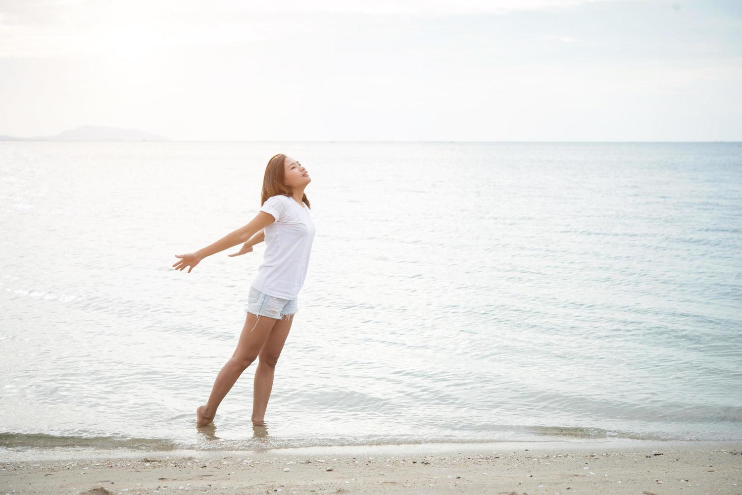 Hermosa joven estira sus brazos en el aire en la playa con los pies descalzos foto