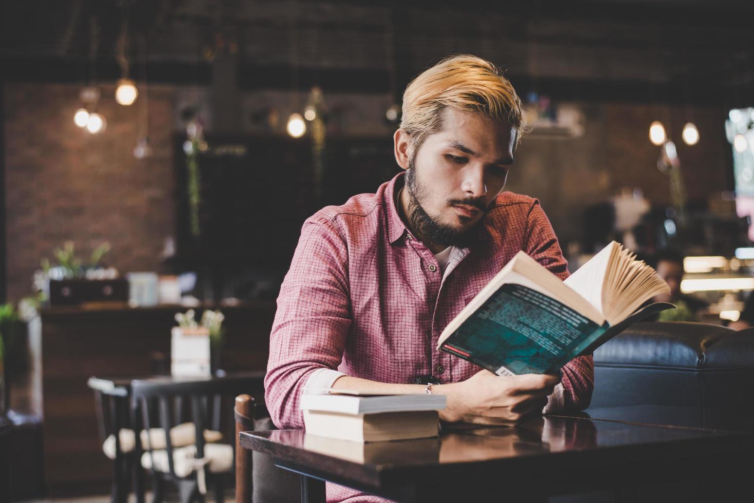 Joven hipster barbudo leyendo un libro en un café foto