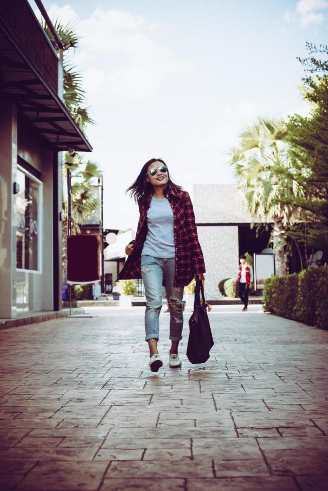 Retrato de mujer joven inconformista con estilo caminando por la calle urbana, sonriendo disfrutar los fines de semana. vintage de hipster adolescente con bolso en mano. foto