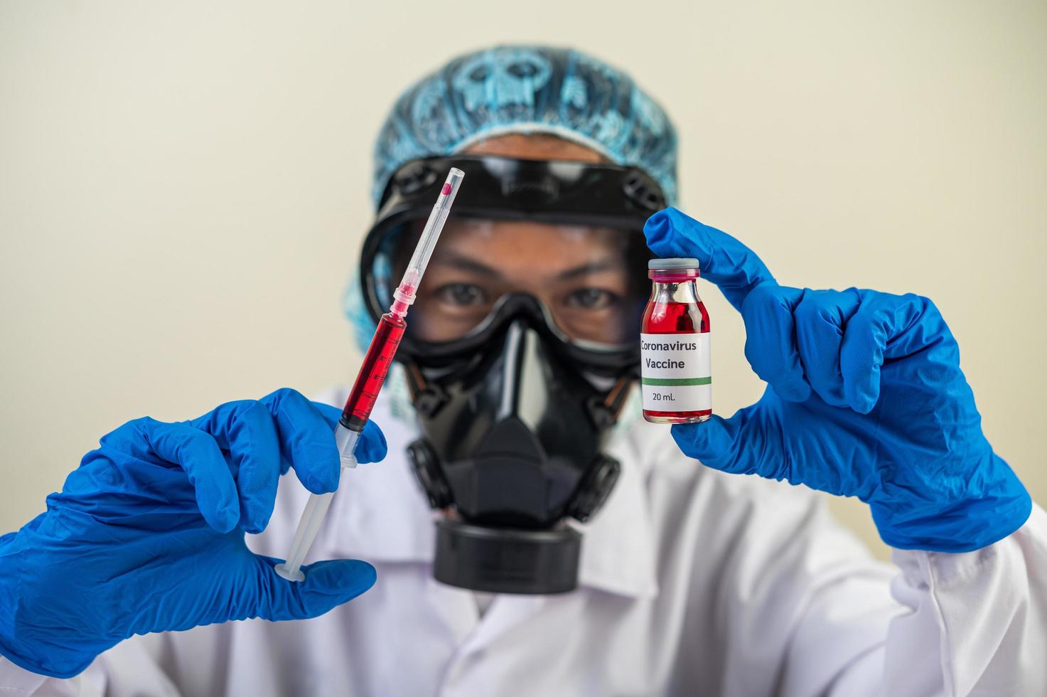 científico con máscaras protectoras y guantes sosteniendo una jeringa con una vacuna para prevenir la covid-19 foto