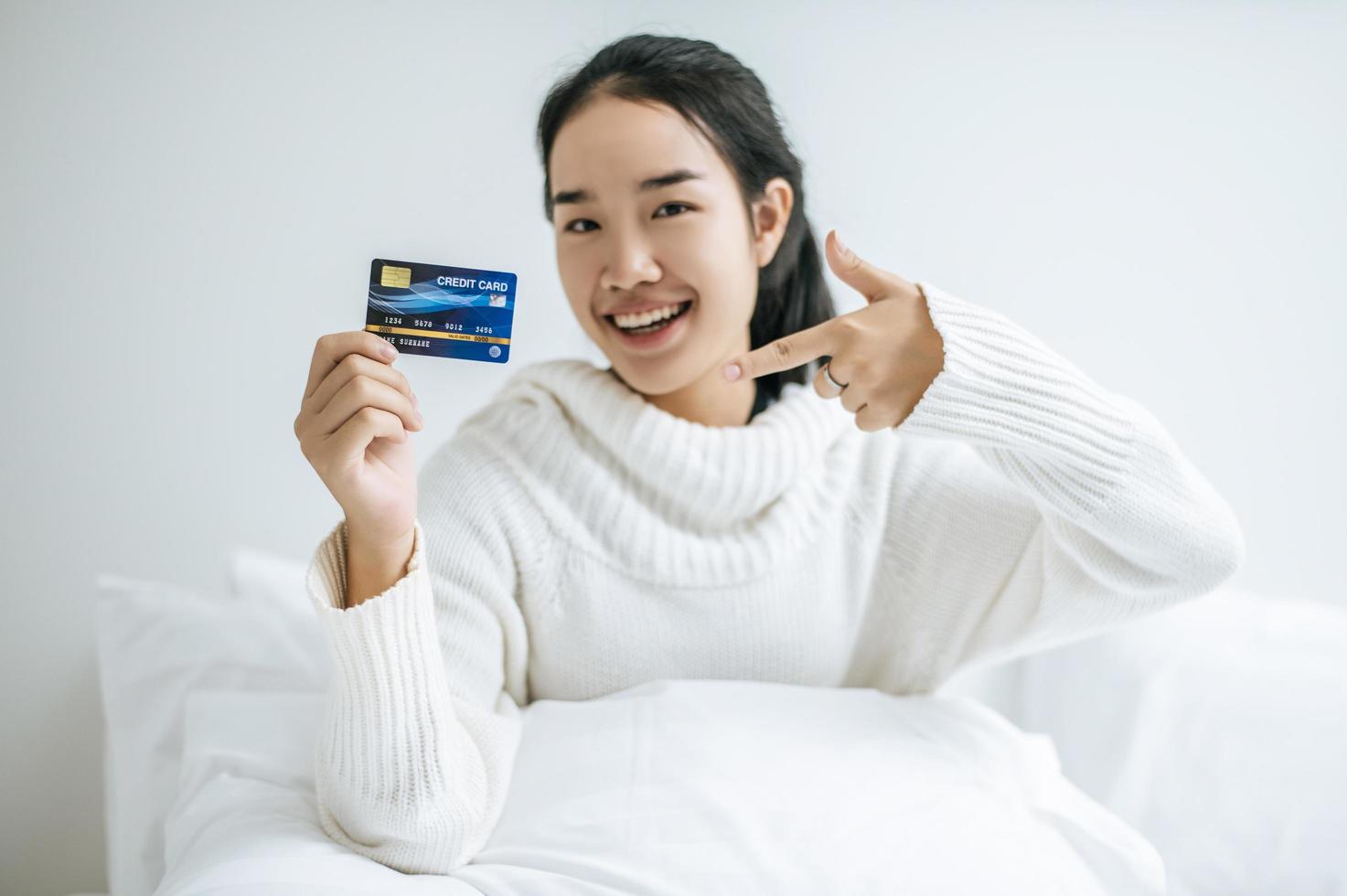 Mujer joven con una tarjeta de crédito sonriendo en la cama foto