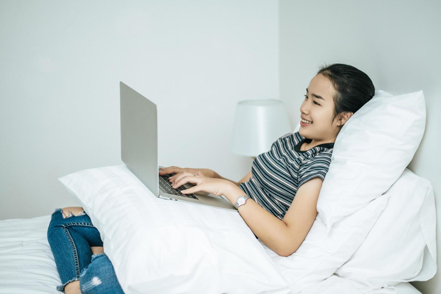 A woman wearing a striped shirt playing on her laptop on her bed photo