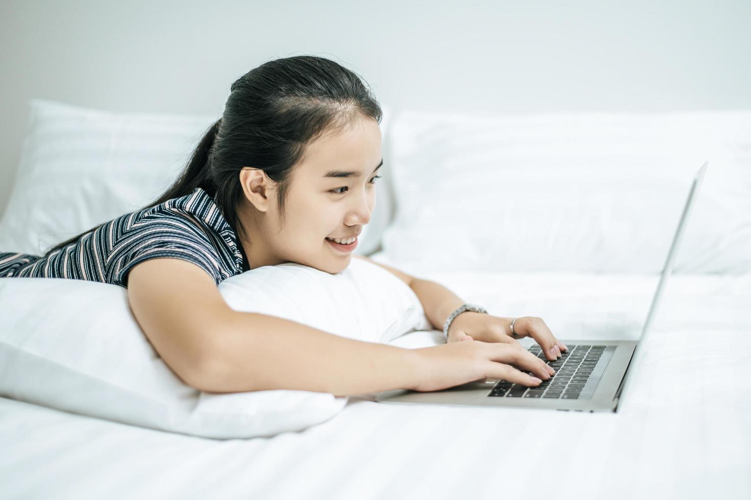 A woman wearing a striped shirt playing on her laptop on her bed photo