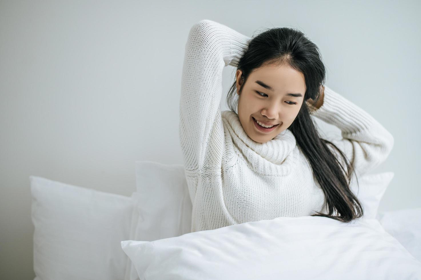 Young woman sits on her bed with both hands raised photo