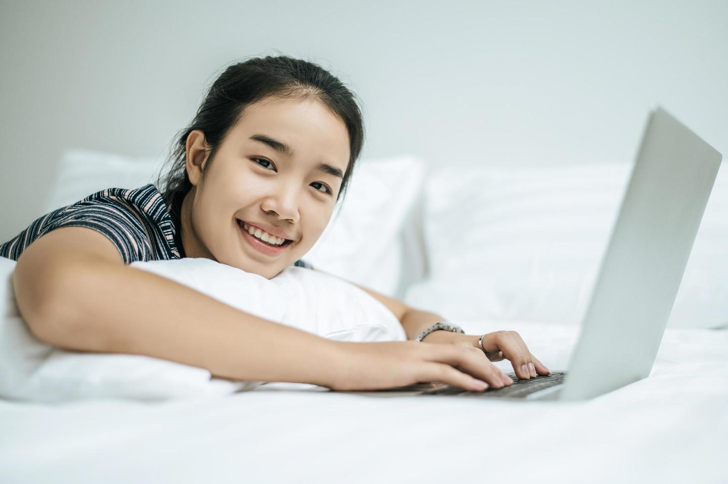 Una mujer vistiendo una camisa a rayas jugando en su computadora portátil en su cama foto