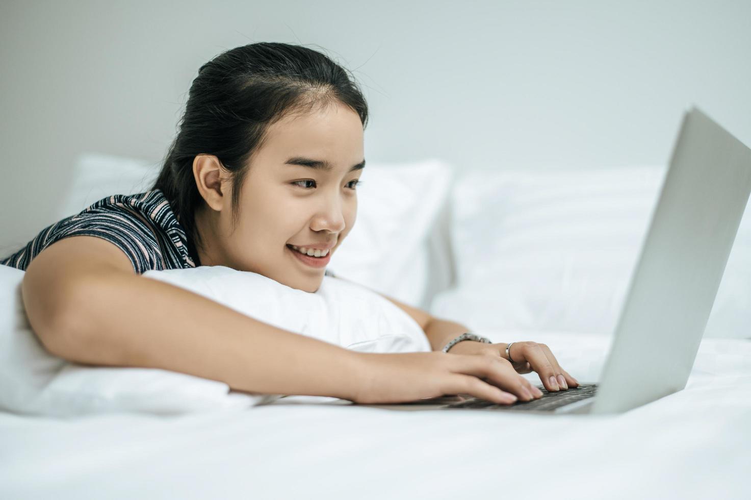 A woman wearing a striped shirt playing on her laptop on her bed photo