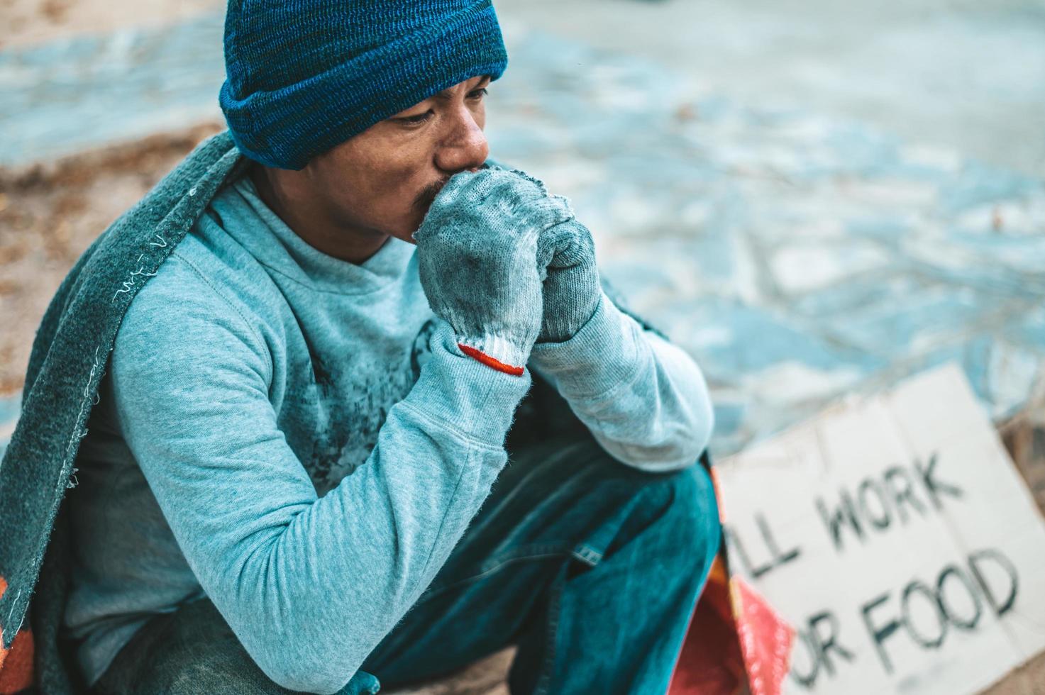 A man sits begging with homeless please help message photo