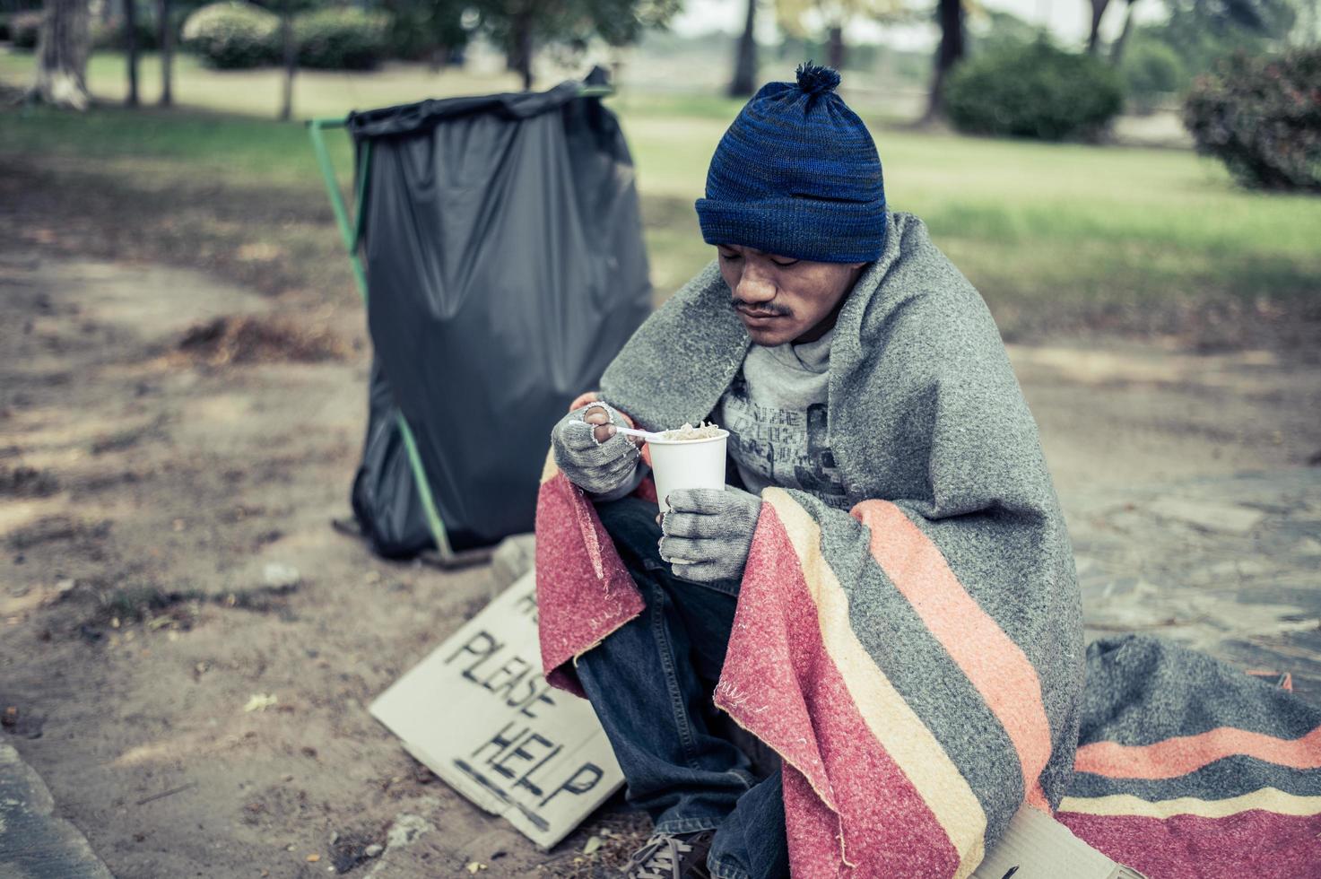 Homeless man wrapped in cloth and eating noodles photo