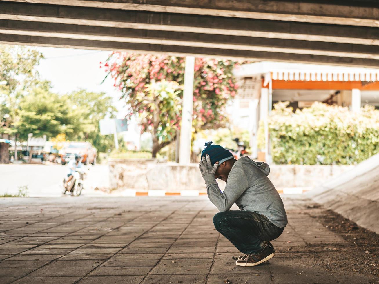 hombre sin hogar se sienta debajo del puente con ambas manos sosteniendo la cabeza foto