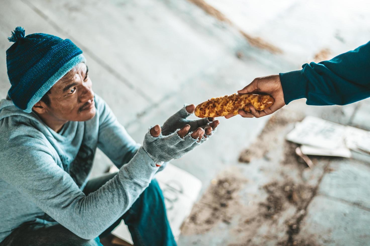 Beggar sitting under an overpass receiving bread from a stranger photo