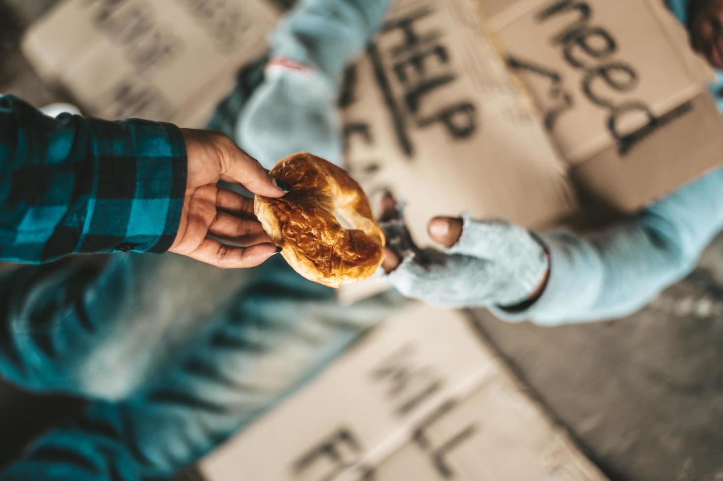 Beggar under the bridge with cardboard help signs accepting bread photo