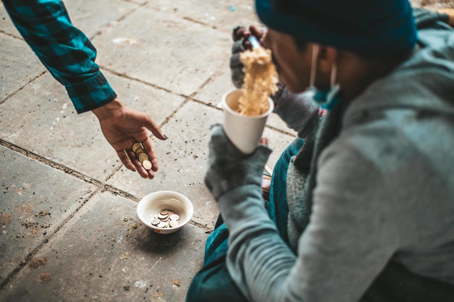 mendigo sentado debajo de un puente con una taza de dinero y fideos foto