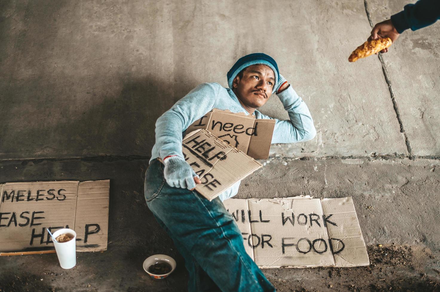 Beggar under the bridge with cardboard help signs accepting bread photo