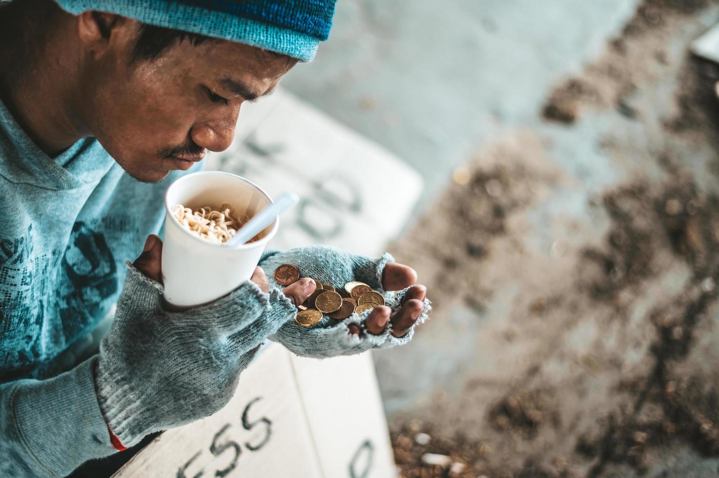 mendigo debajo del puente con una taza que contiene monedas y fideos instantáneos foto