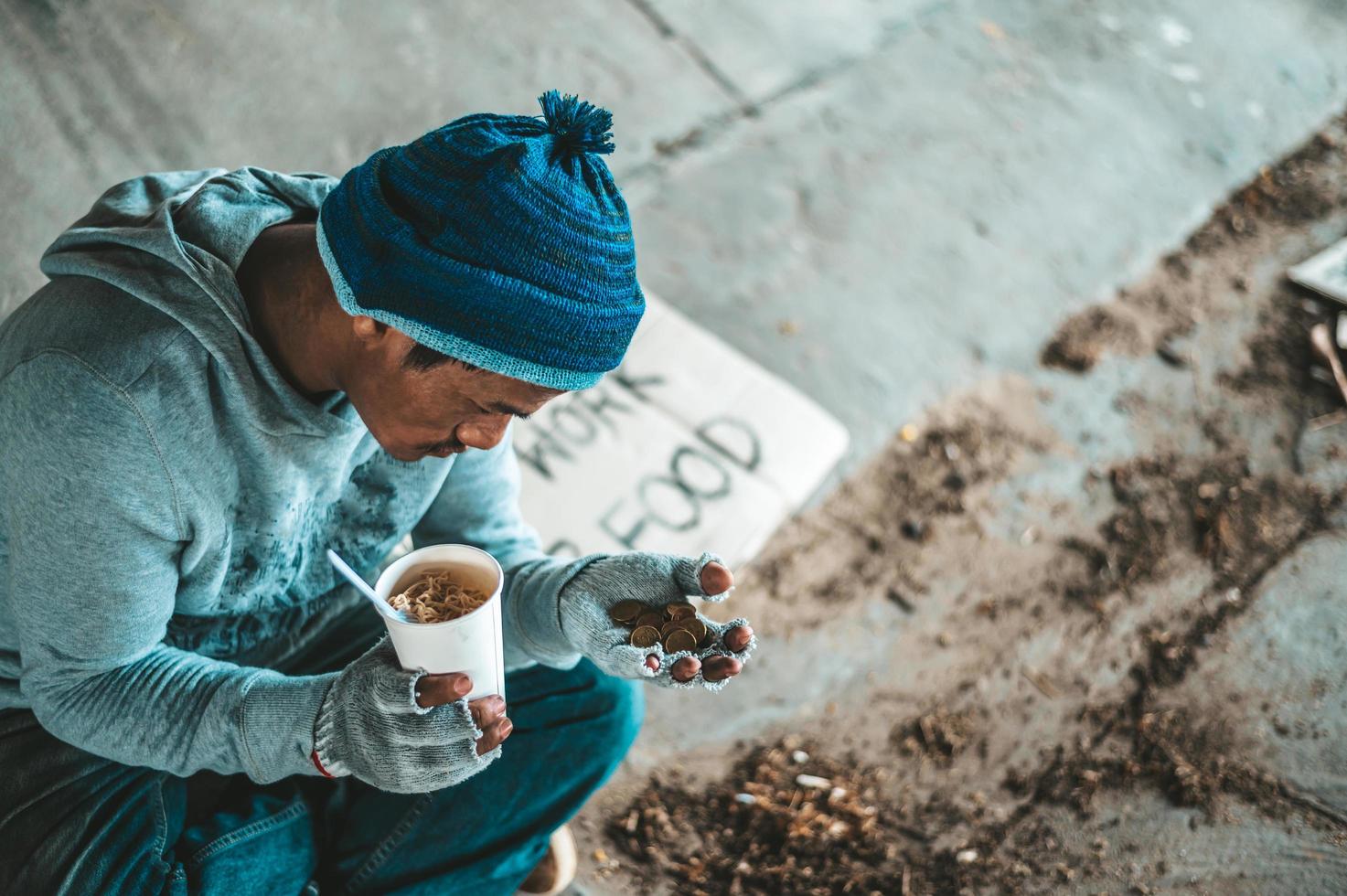 mendigo debajo del puente con una taza que contiene monedas y fideos instantáneos foto