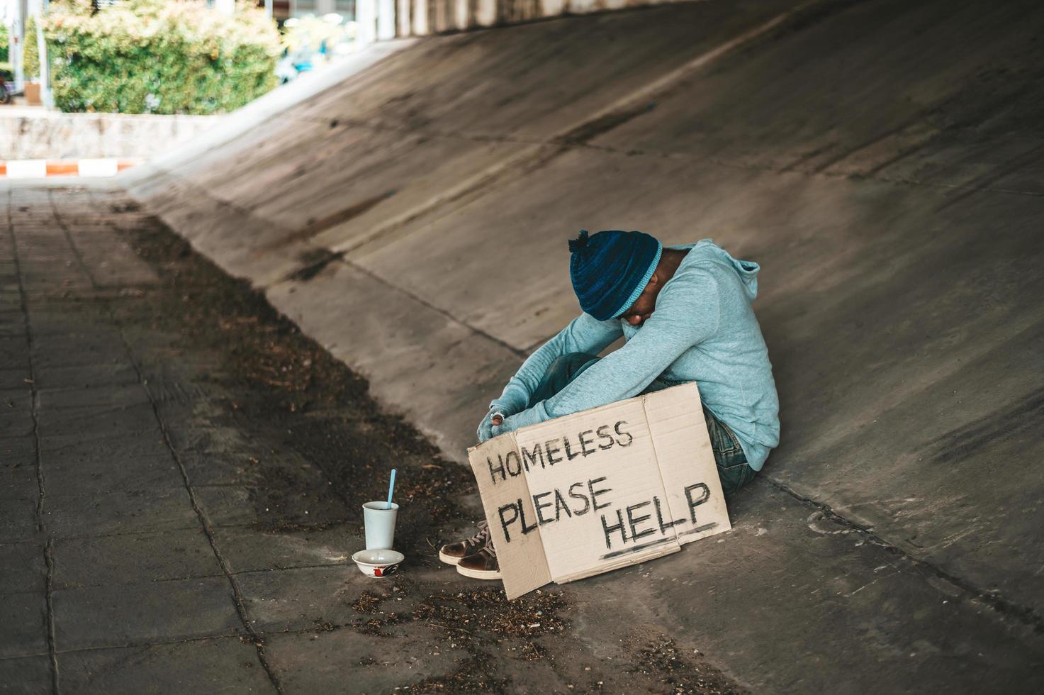 mendigo sentado debajo de un puente con una taza de dinero y fideos foto