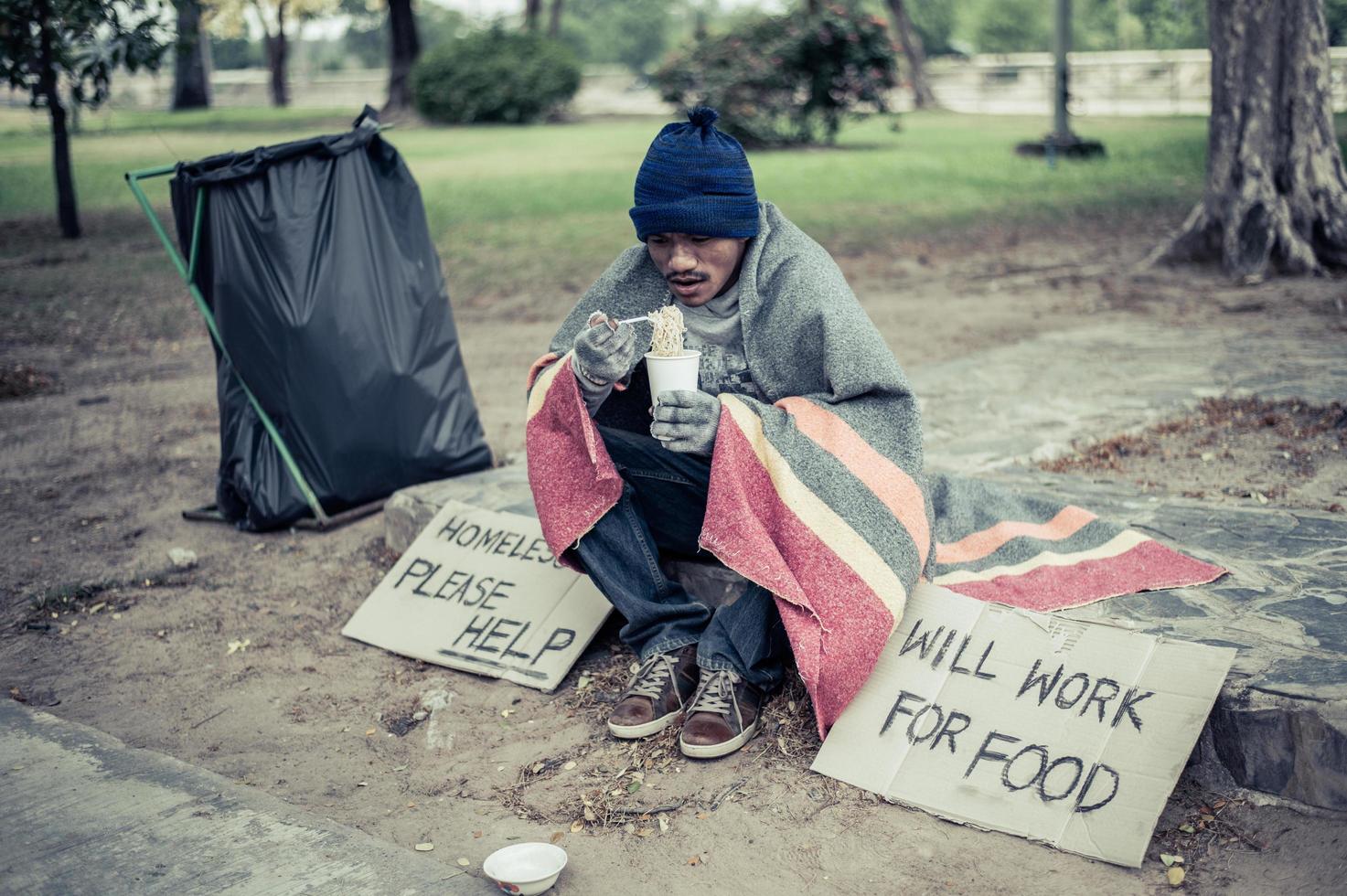 Hombre sin hogar envuelto en tela y comiendo fideos foto