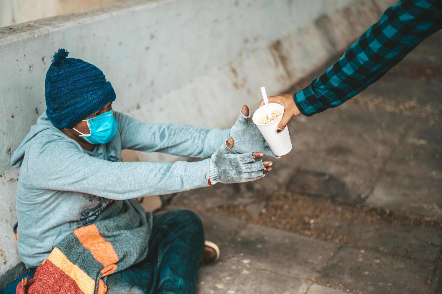 Beggar sitting under the overpass and accepting noodles from someone photo