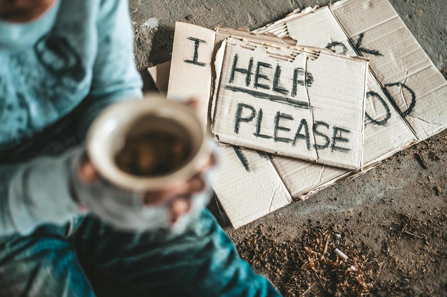 mendigo sentado debajo de un puente con una taza de dinero foto