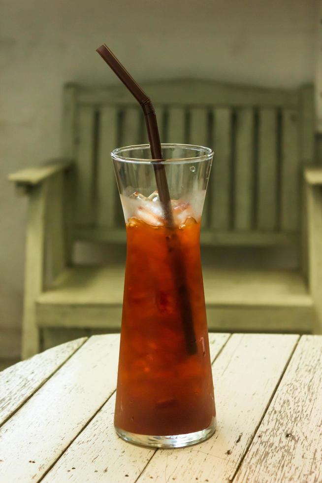 Glass of iced tea with straw on wood table photo