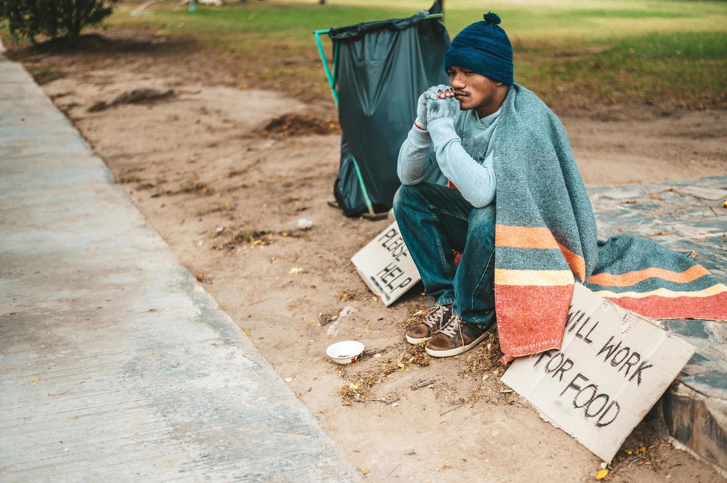 un mendigo sentado afuera con carteles de ayuda foto