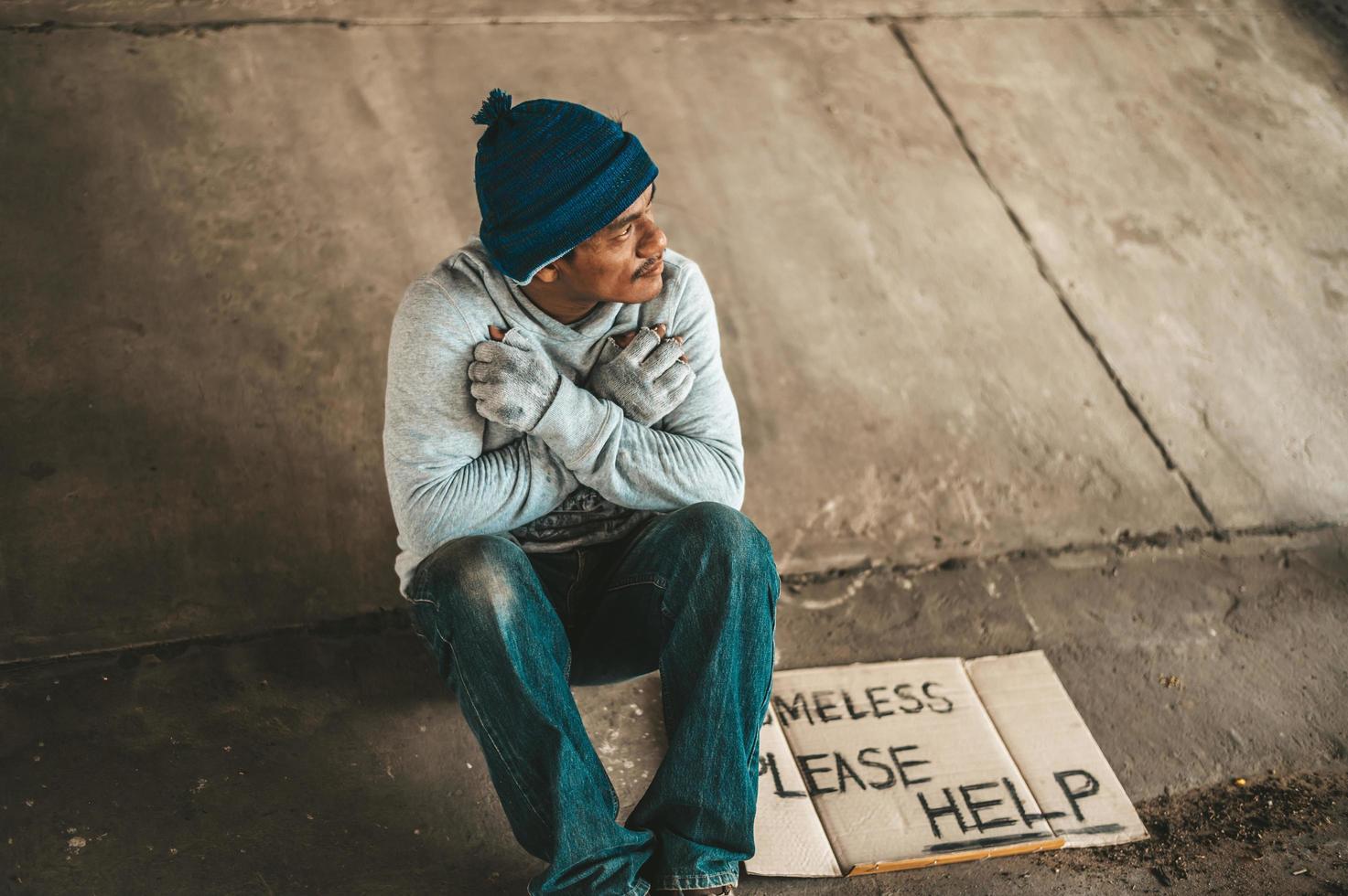 Beggar sitting under the overpass with a please help sign photo