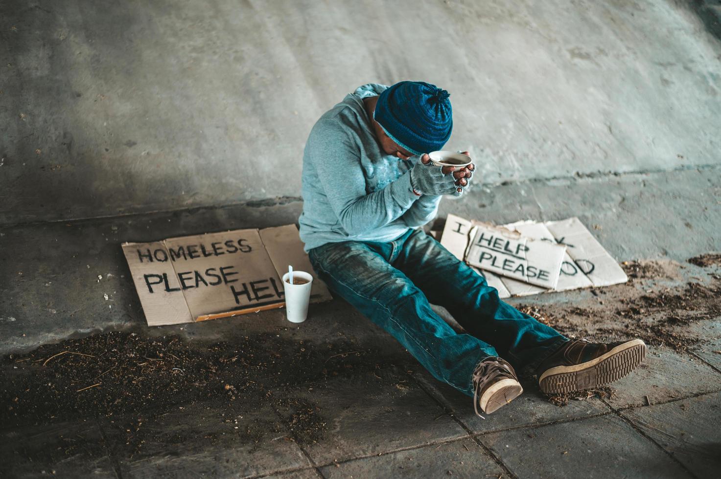 mendigo sentado debajo de un puente con una taza de dinero foto
