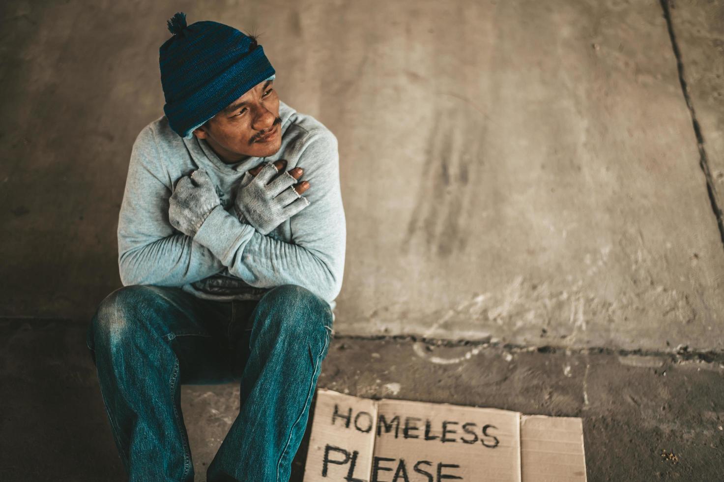 Beggar sitting under the overpass with a please help sign photo