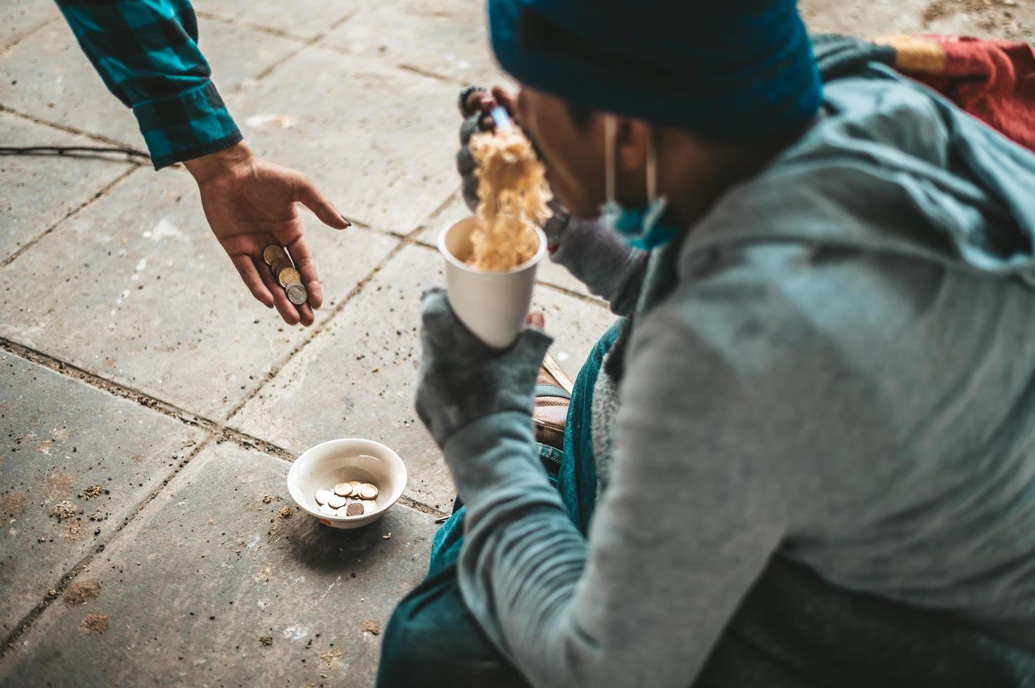 mendigo sentado debajo de un puente con una taza de dinero y fideos foto