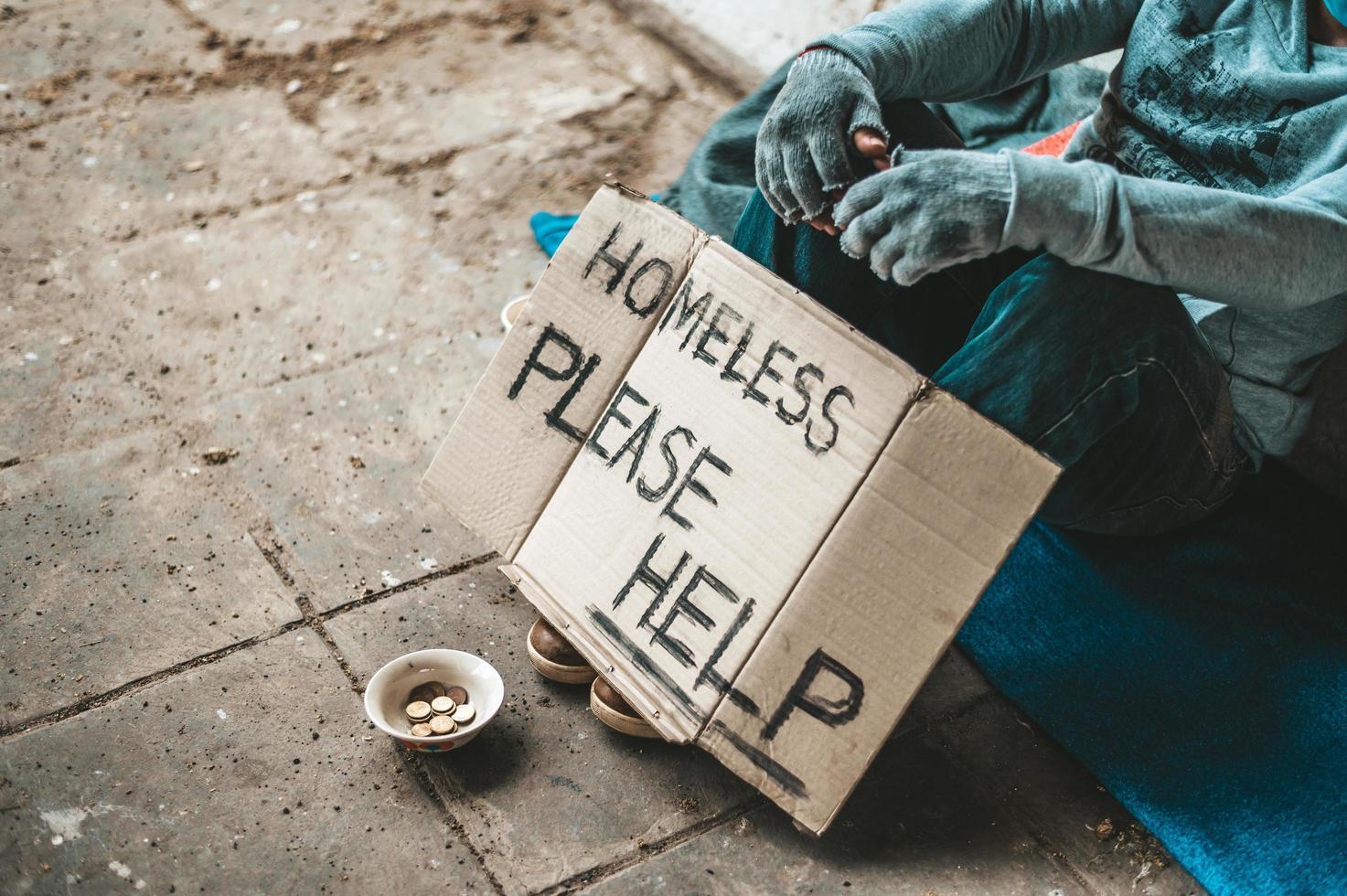 Man sits beside the street with a homeless message photo