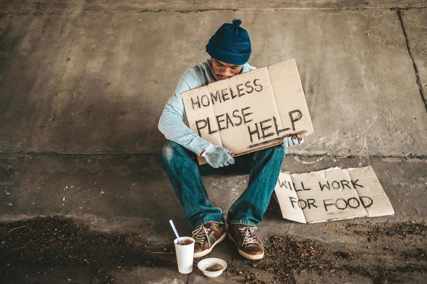 Beggar sitting under the overpass with a please help sign photo