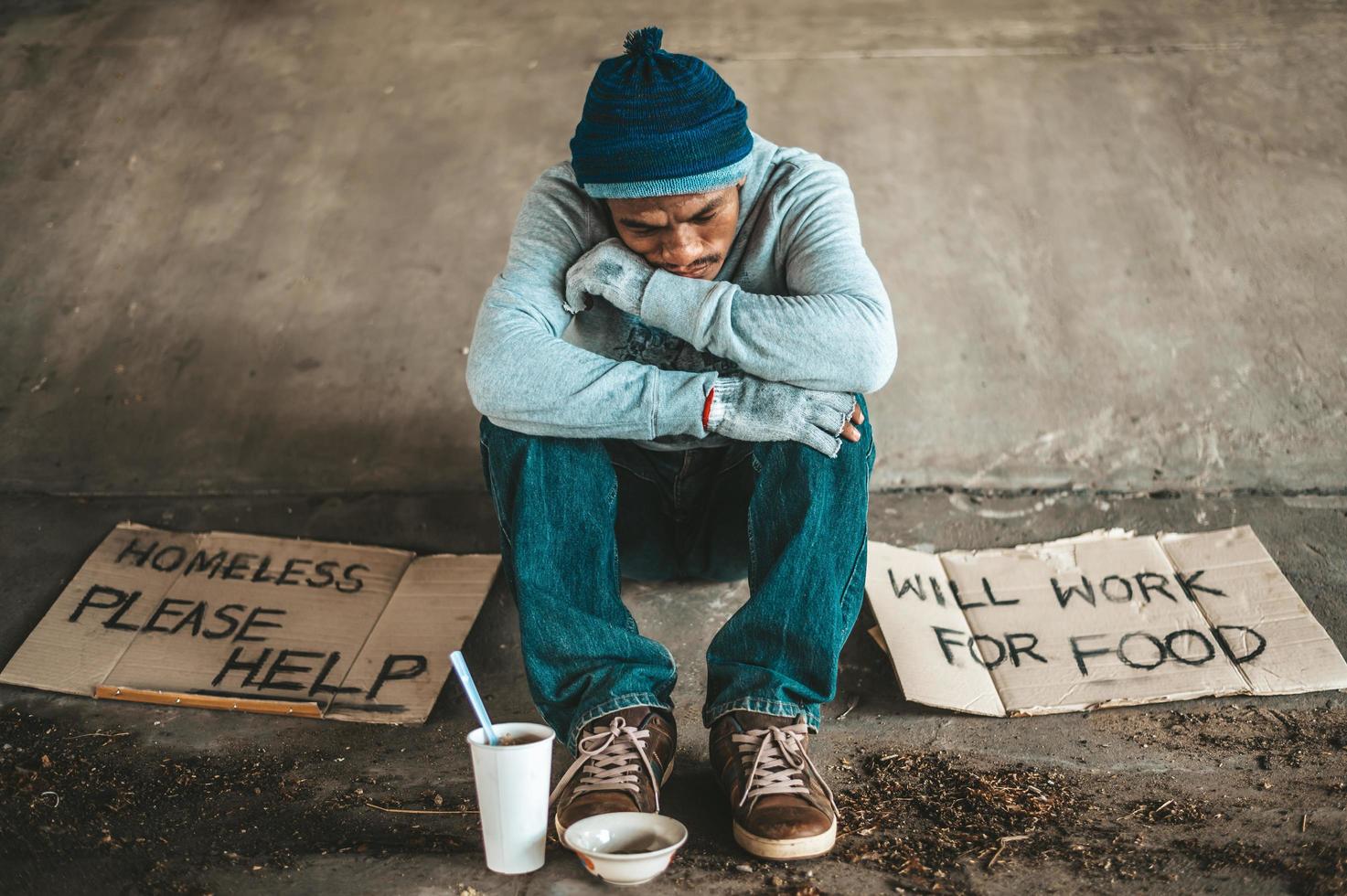 Beggar sitting under the overpass with a please help sign photo