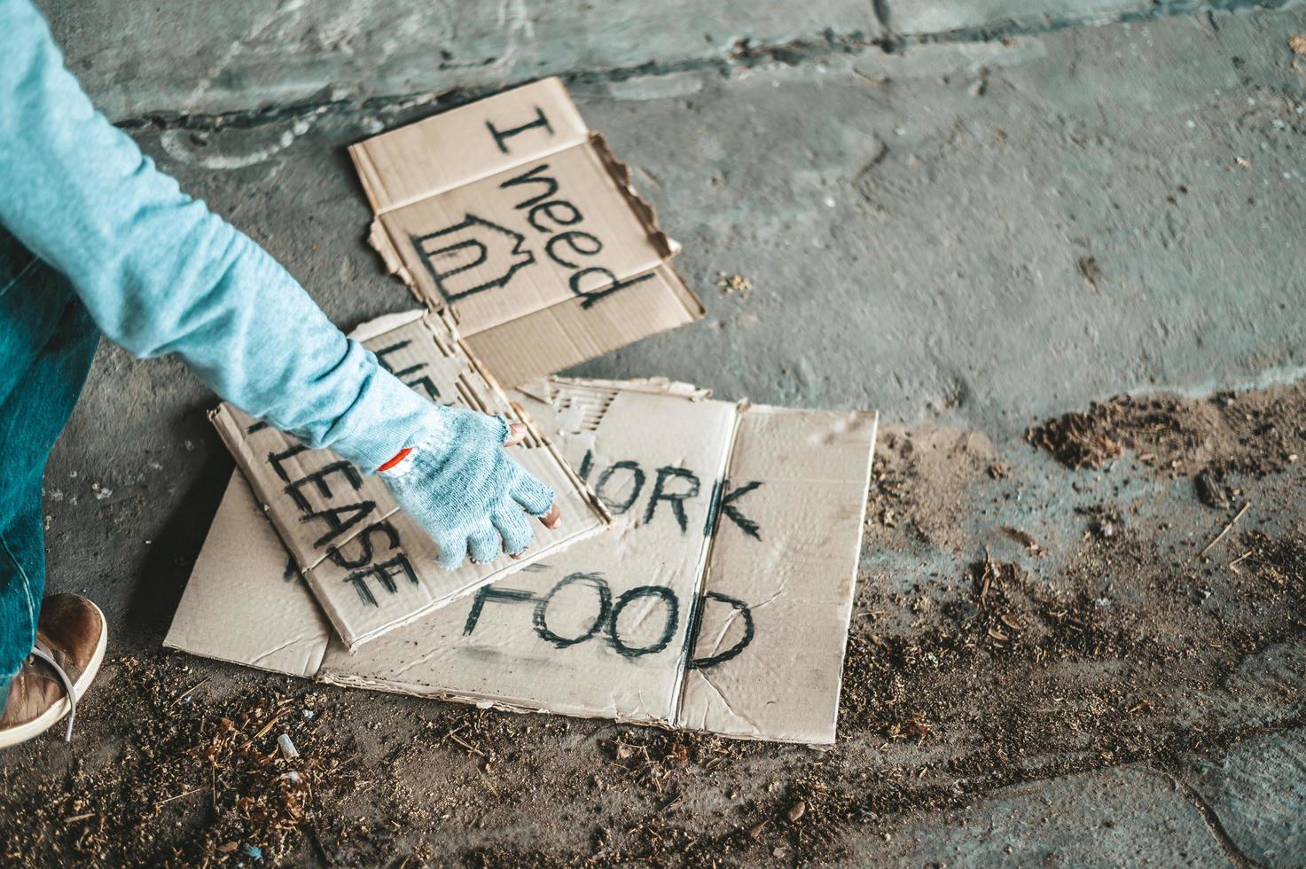 Beggar sitting under a bridge with cardboard signs for help photo