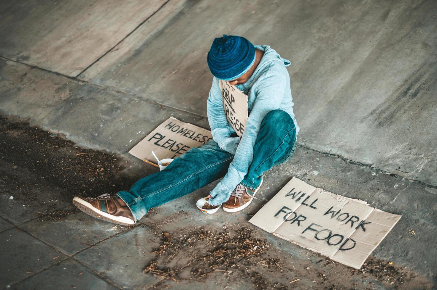 Beggar under the bridge with a cup of instant noodles and a help sign photo