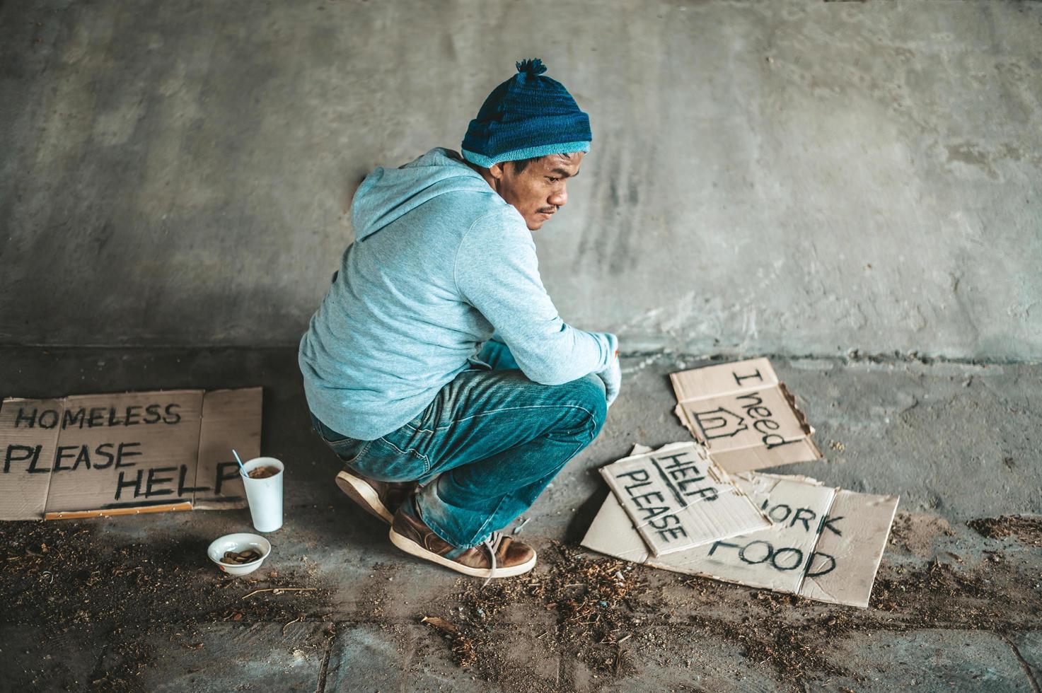Beggar sitting under a bridge with cardboard signs for help photo