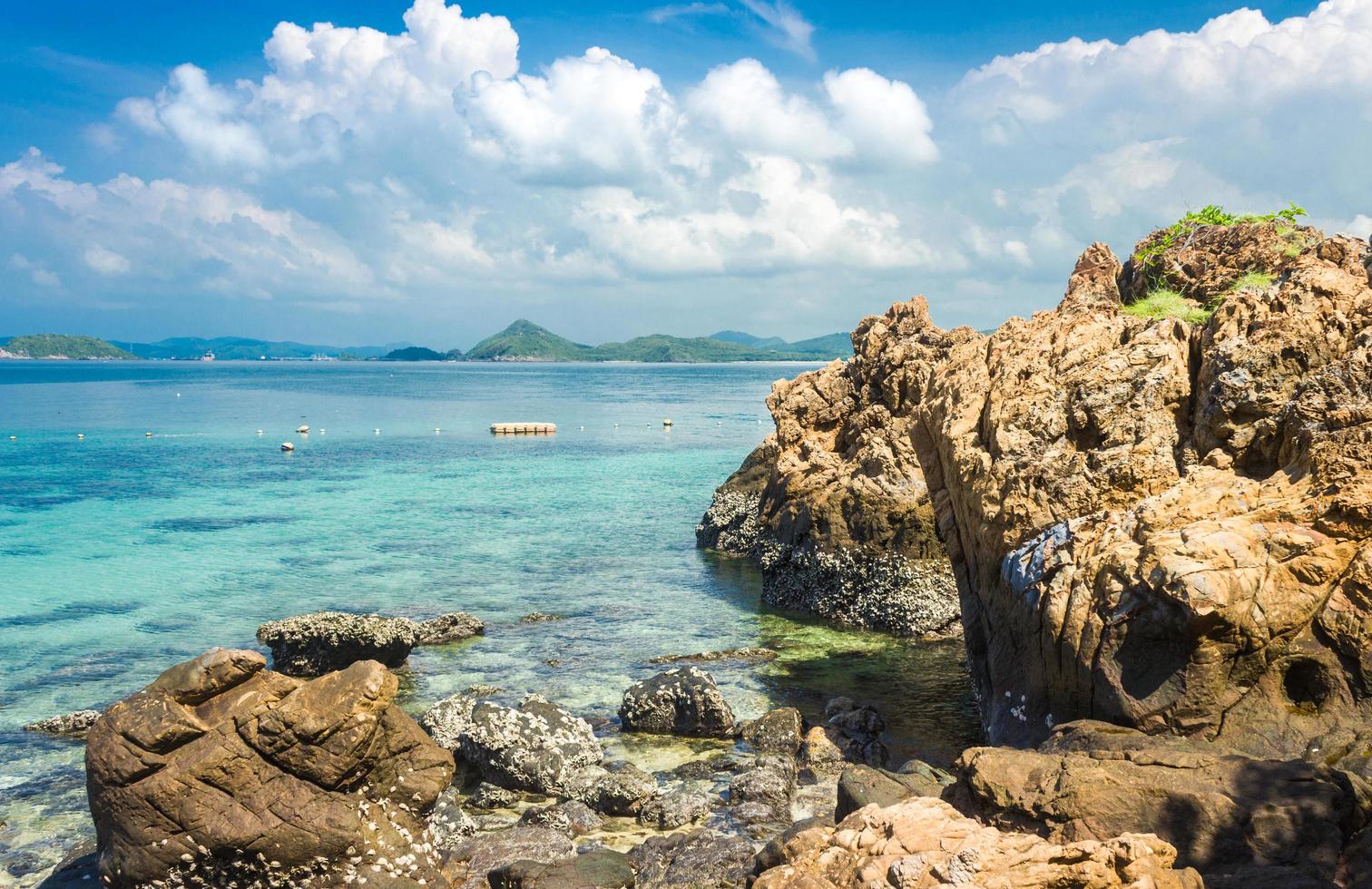 Rocas de la isla tropical en la playa por agua con nublado cielo azul foto