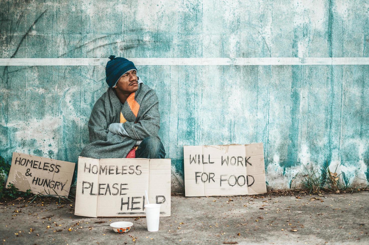 El hombre se sienta al lado de la calle con un mensaje para personas sin hogar. foto