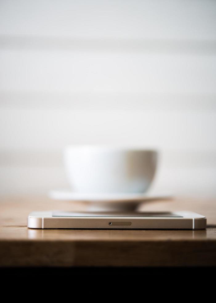 A cup of coffee and smartphone on wooden table in cafe photo