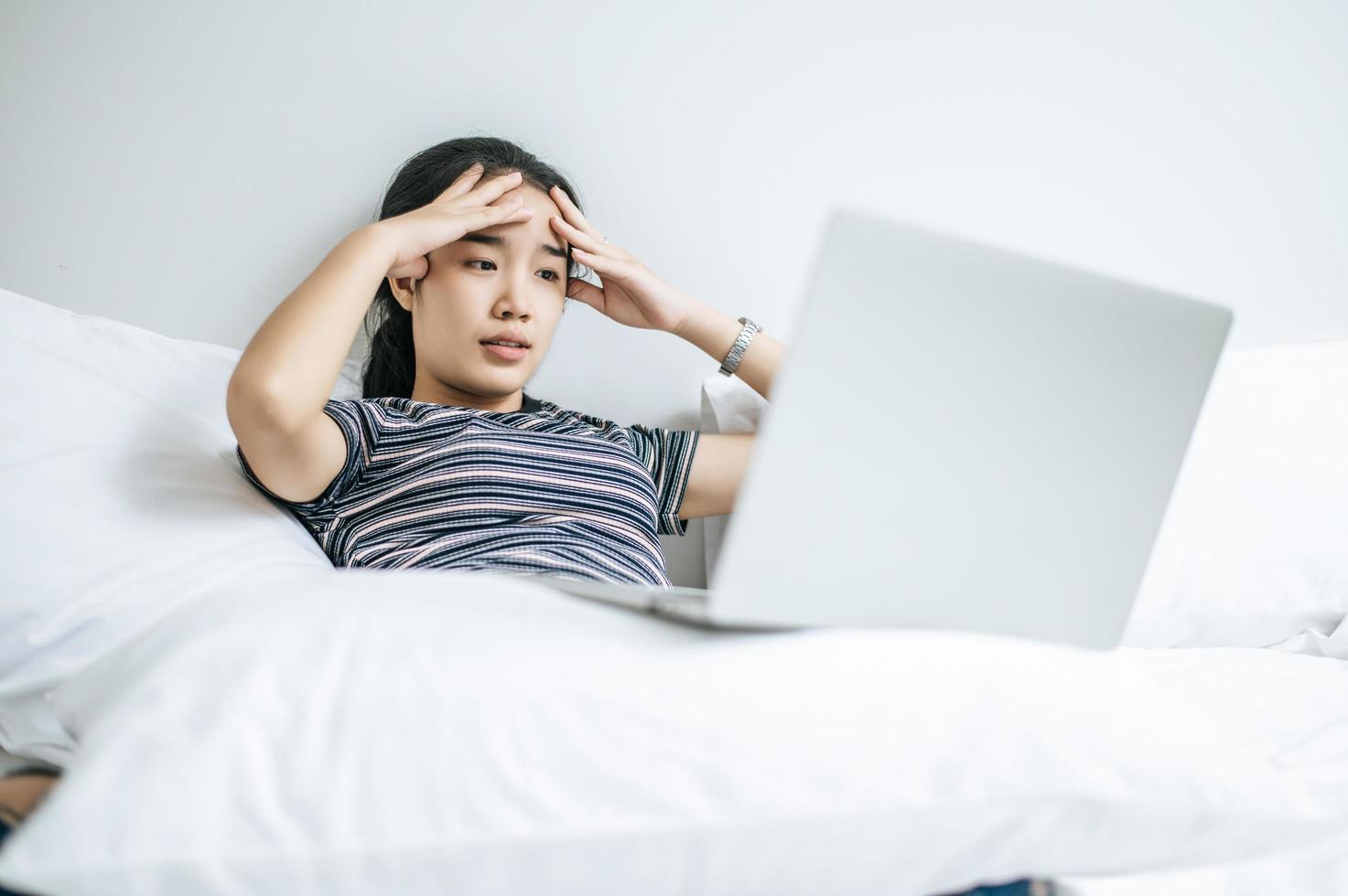 A woman wearing a striped shirt playing on her laptop on her bed photo