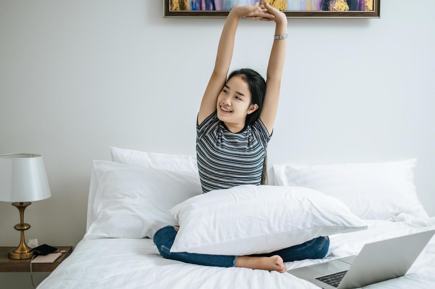 Mujer joven sentada en su cama estirando sus brazos foto