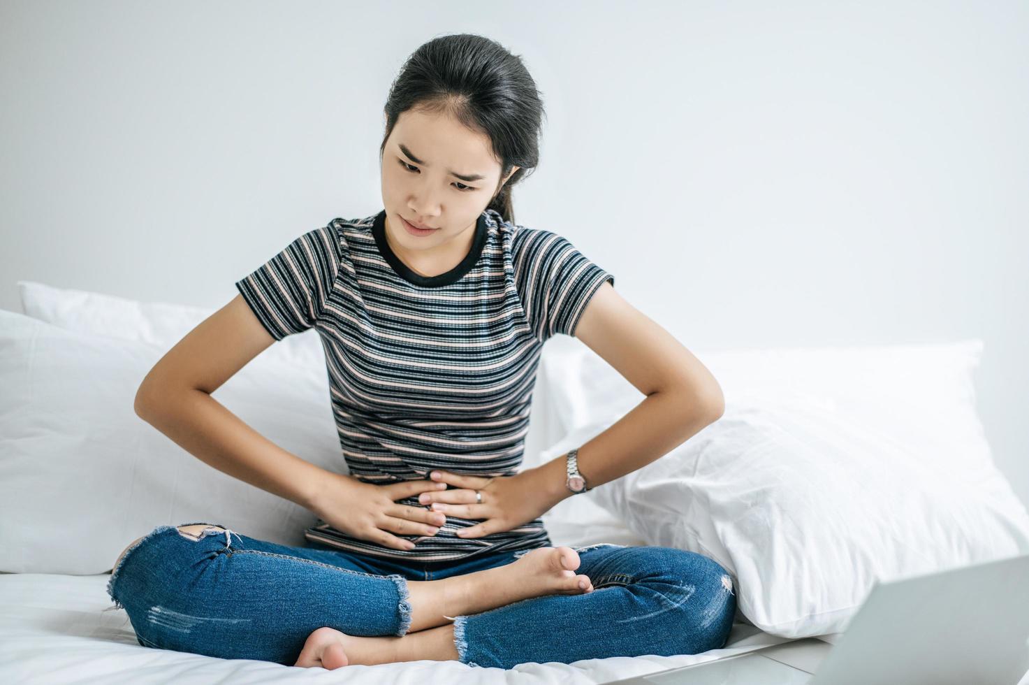 Young woman on her bed with both hands pressed to her stomach photo