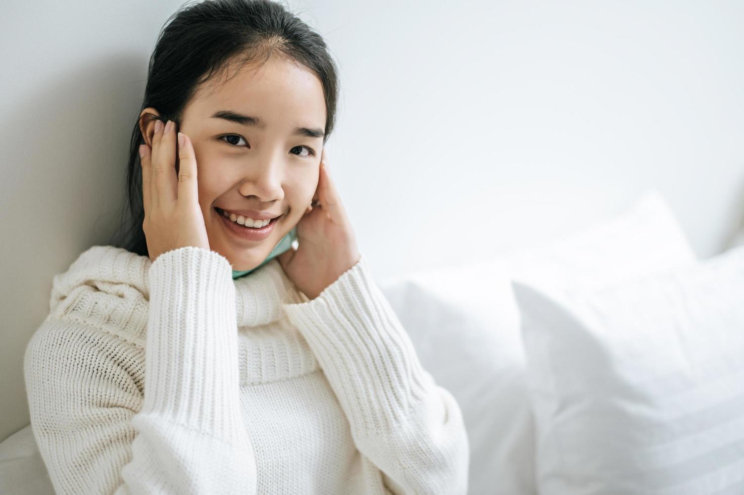 Young woman sitting on her bed with hands touching cheeks photo