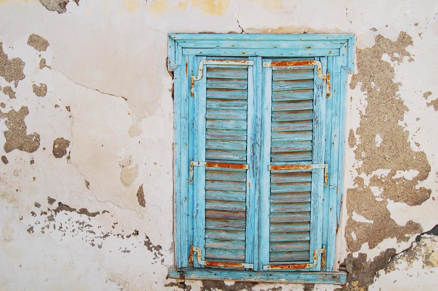 Ventana de persiana de madera azul en una pared con pintura gris desconchada foto