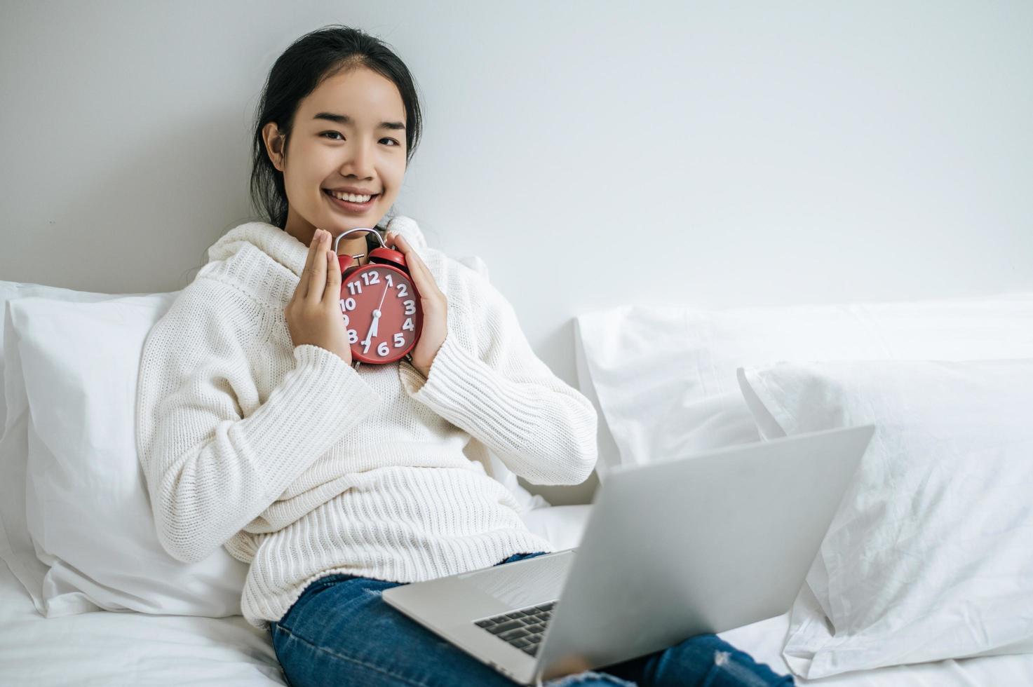 Mujer joven sentada en su cama sosteniendo un reloj despertador foto