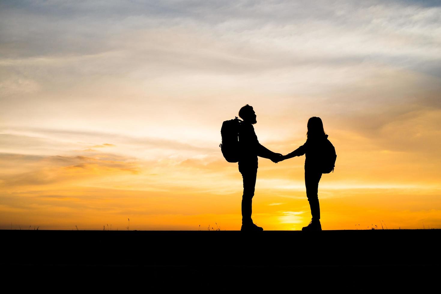 Silhouettes of two hikers with backpacks enjoying the sunset photo