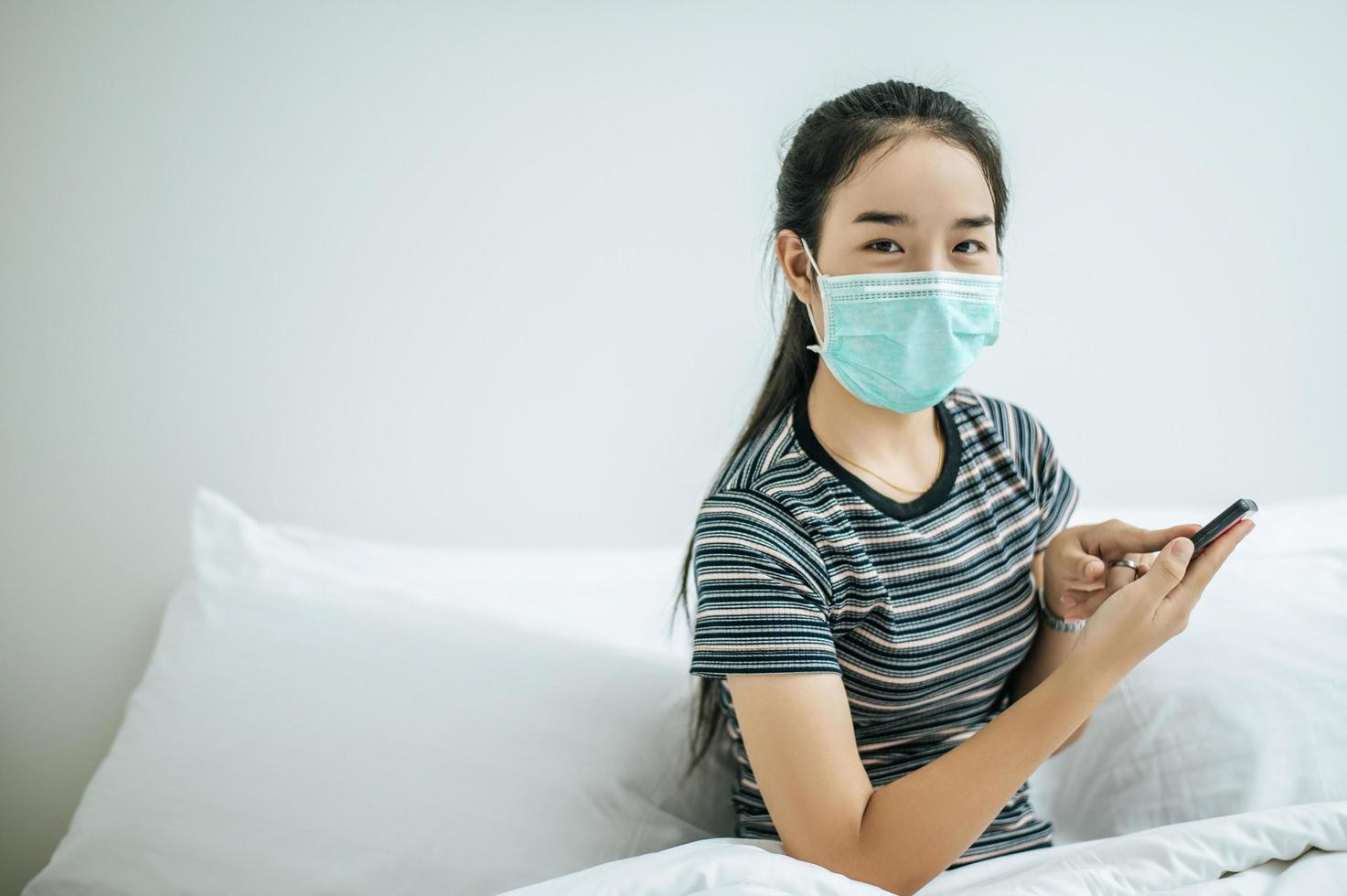 Girl wearing a sanitation mask, striped shirt and holding a mobile phone photo